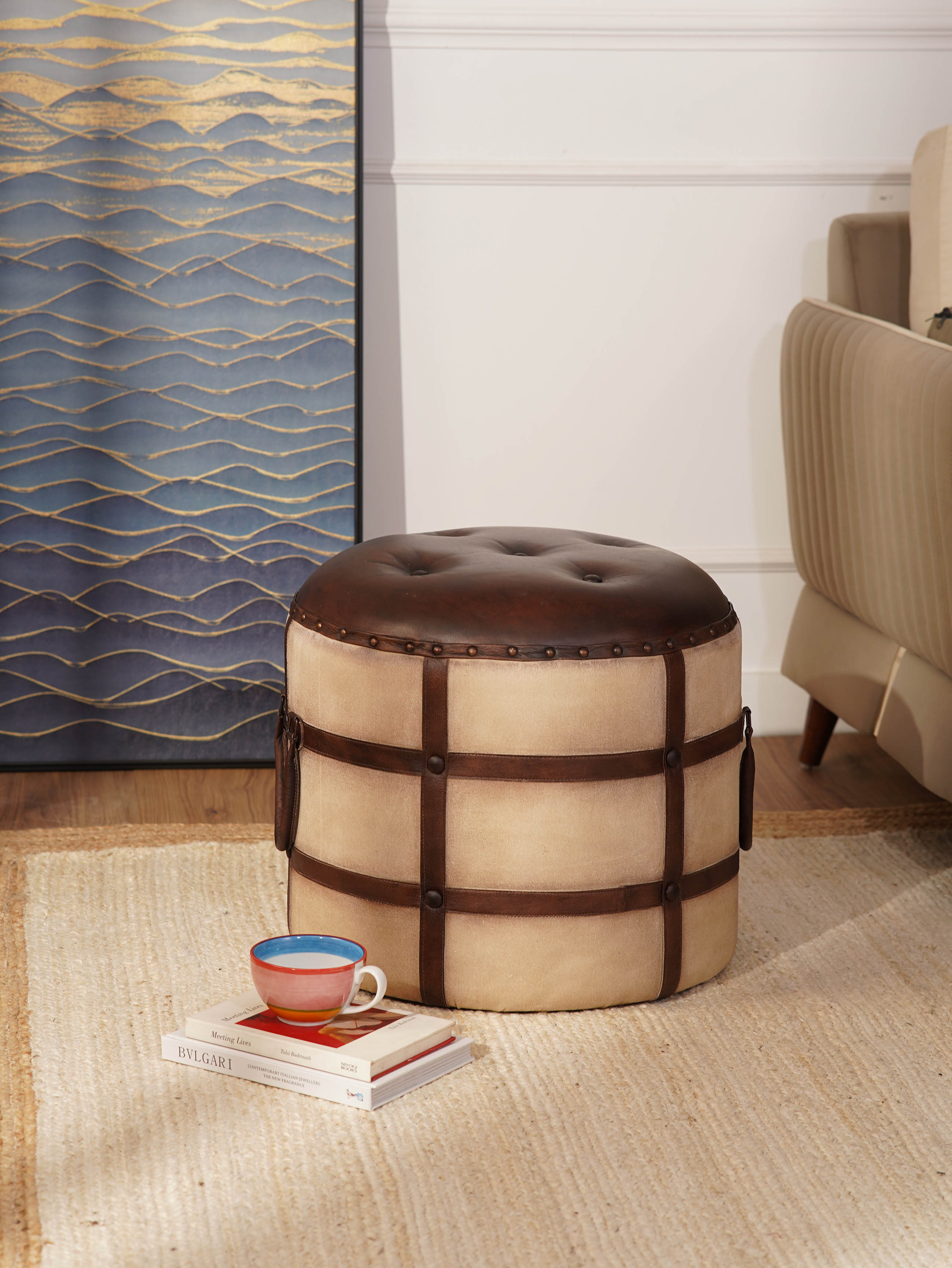 Round ottoman with canvas and leather upholstery beside beige armchair