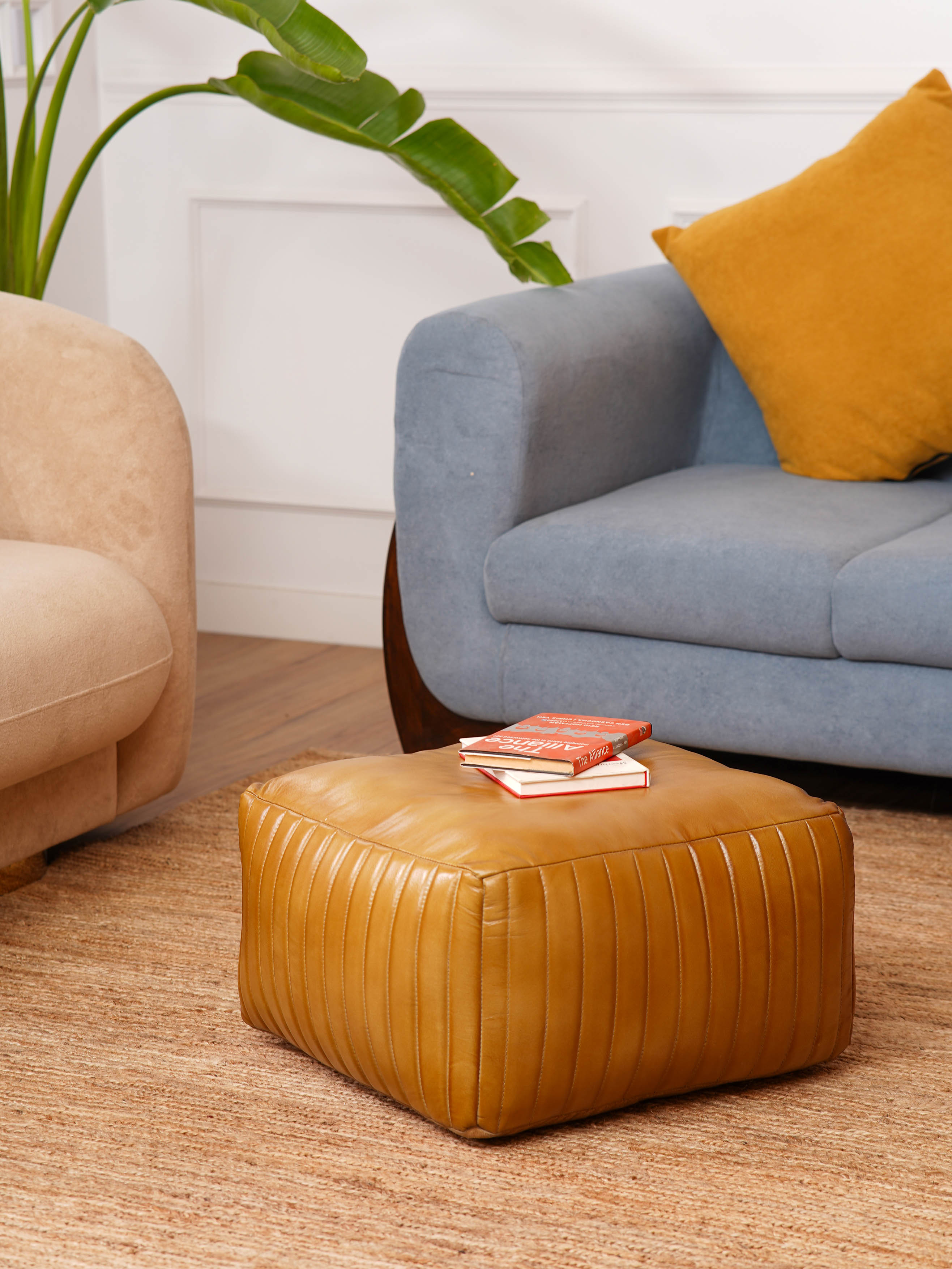 Beige square leather pouf styled beside modern blue armchair and tan chair