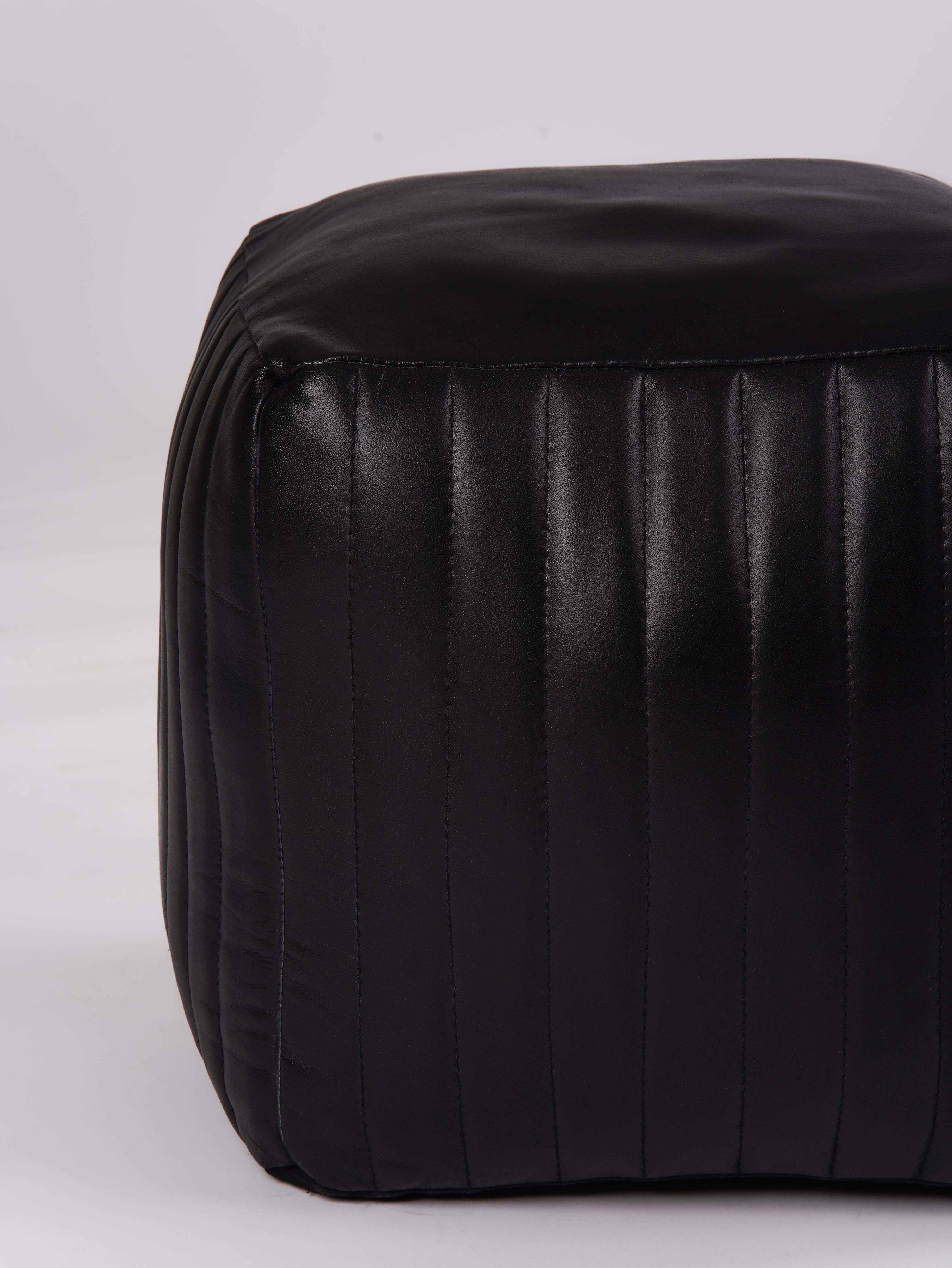 Side view of black leather pouf with vertical stitched panels