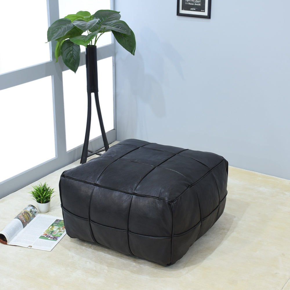 Black square leather pouf next to armchair in modern living room