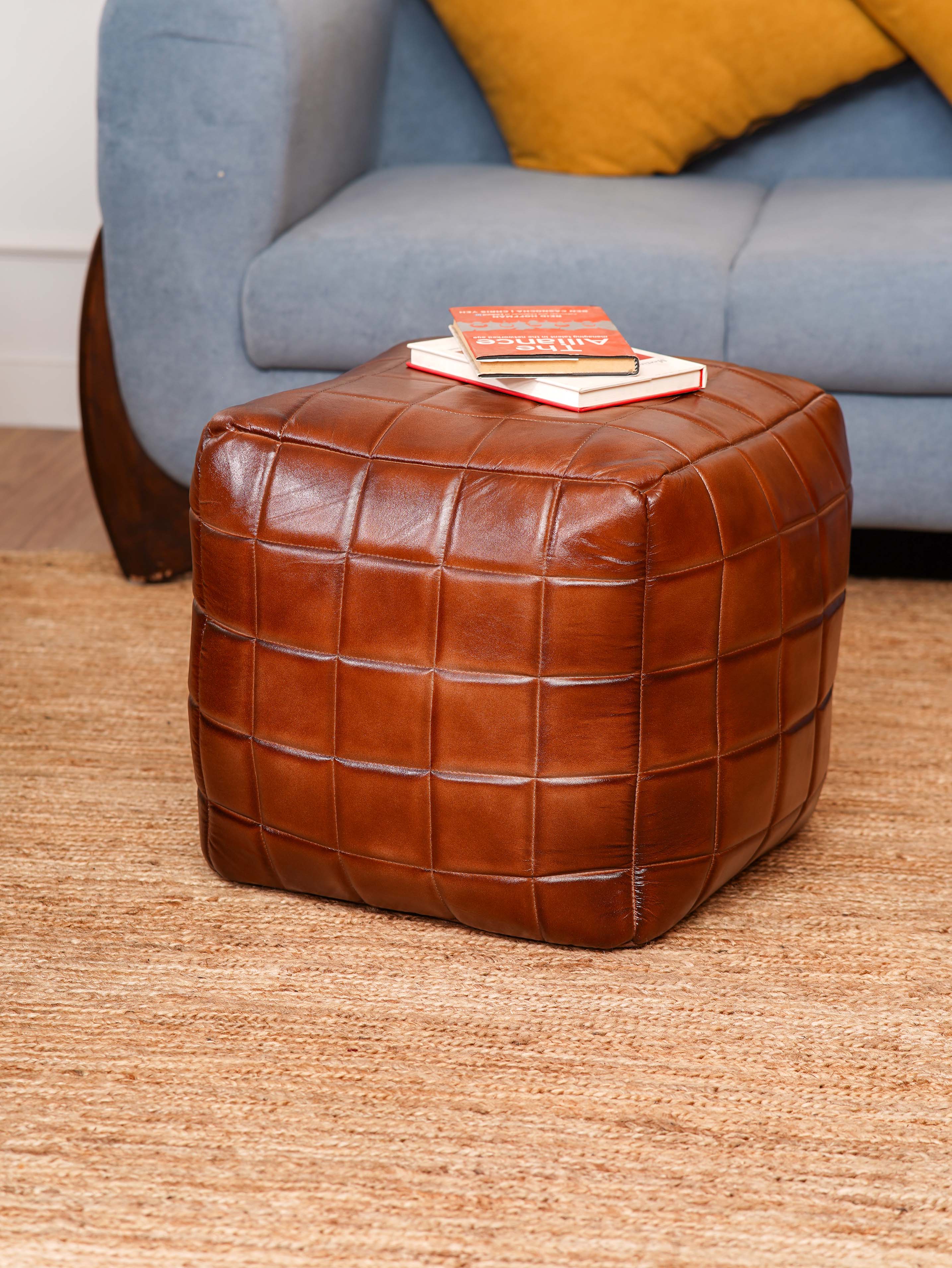 Brown leather square pouf beside modern blue armchair