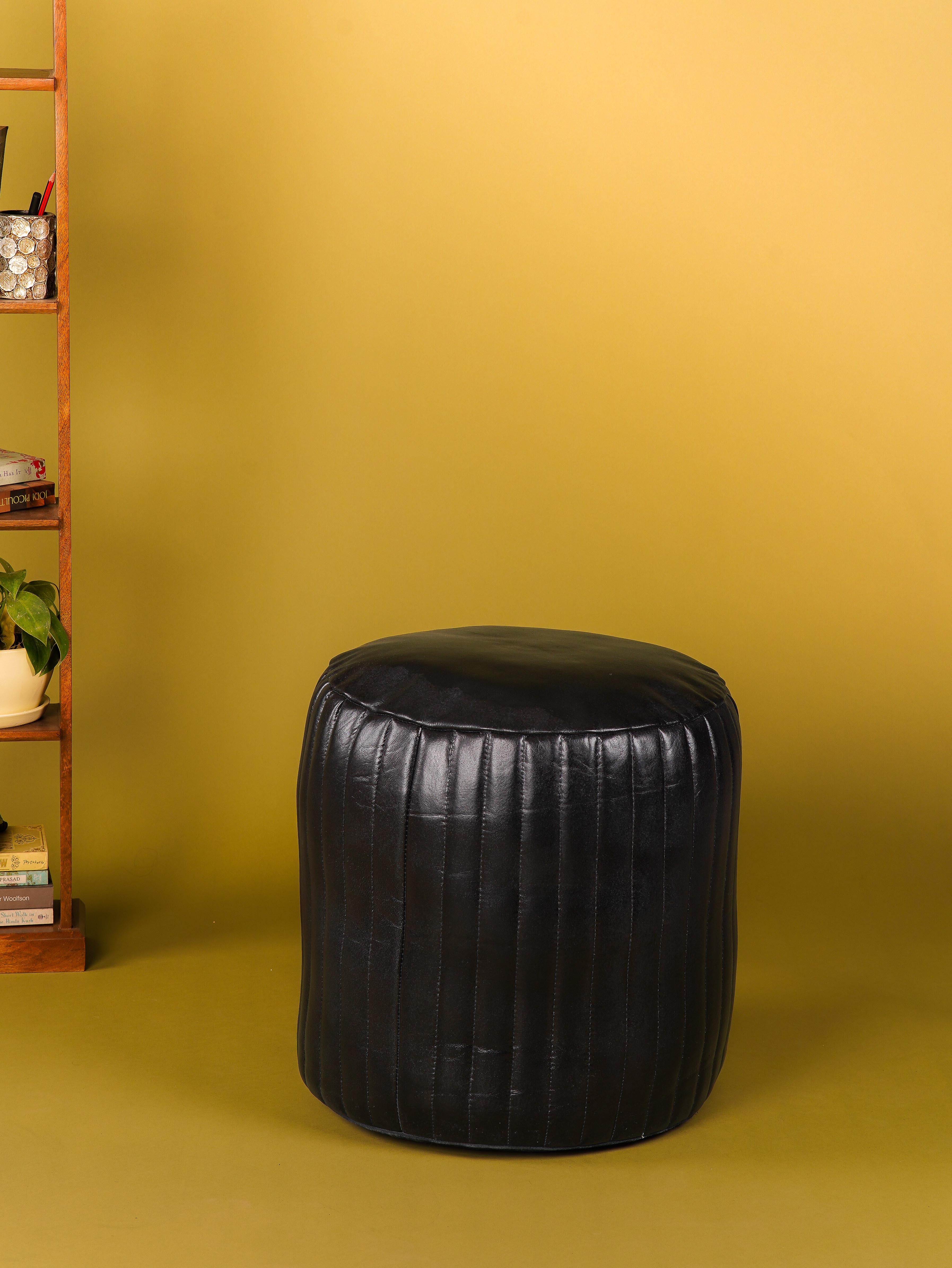 Round black buffalo leather pouf in modern room with yellow backdrop