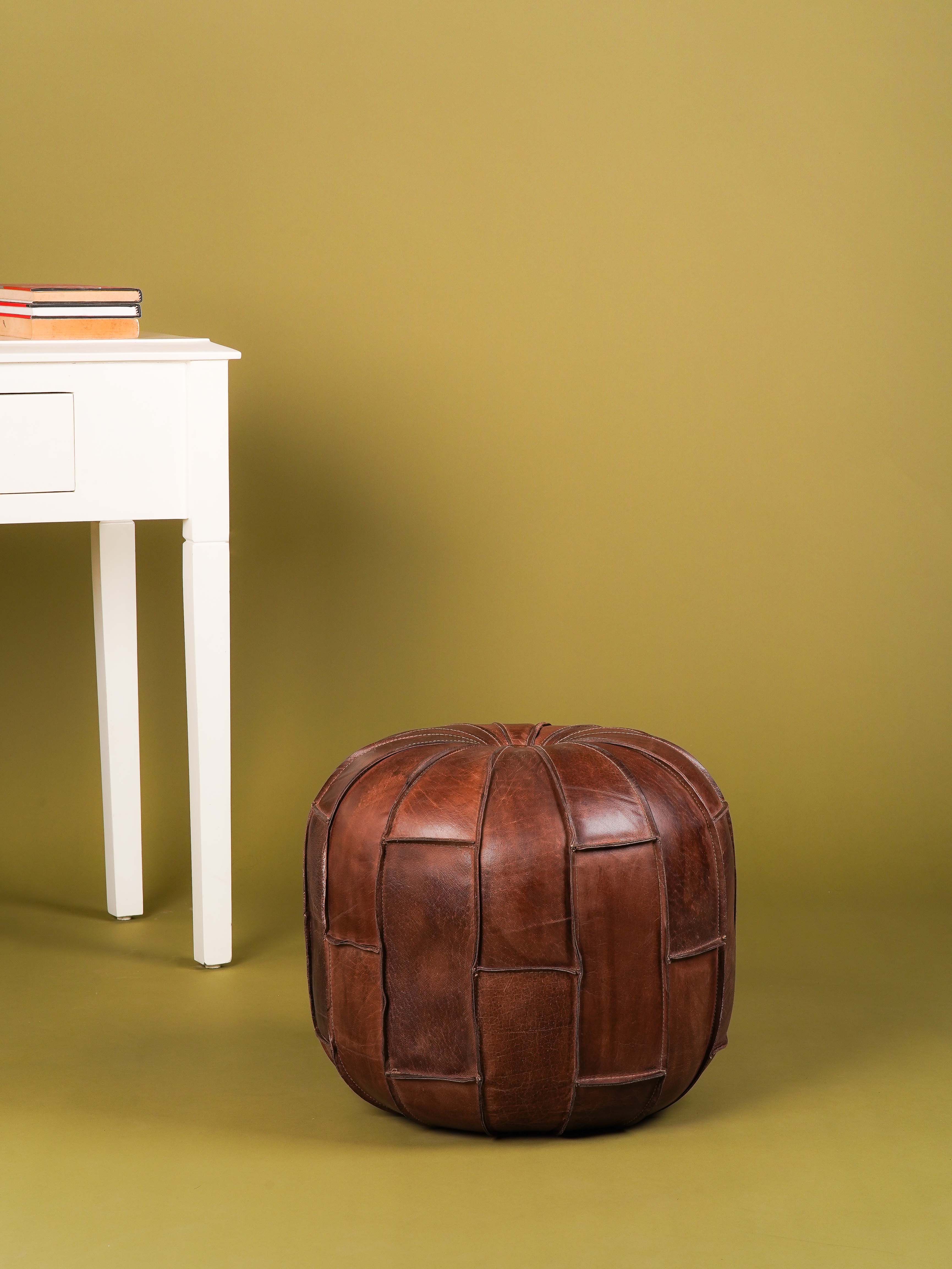 Round black buffalo leather pouf placed in modern living room setting