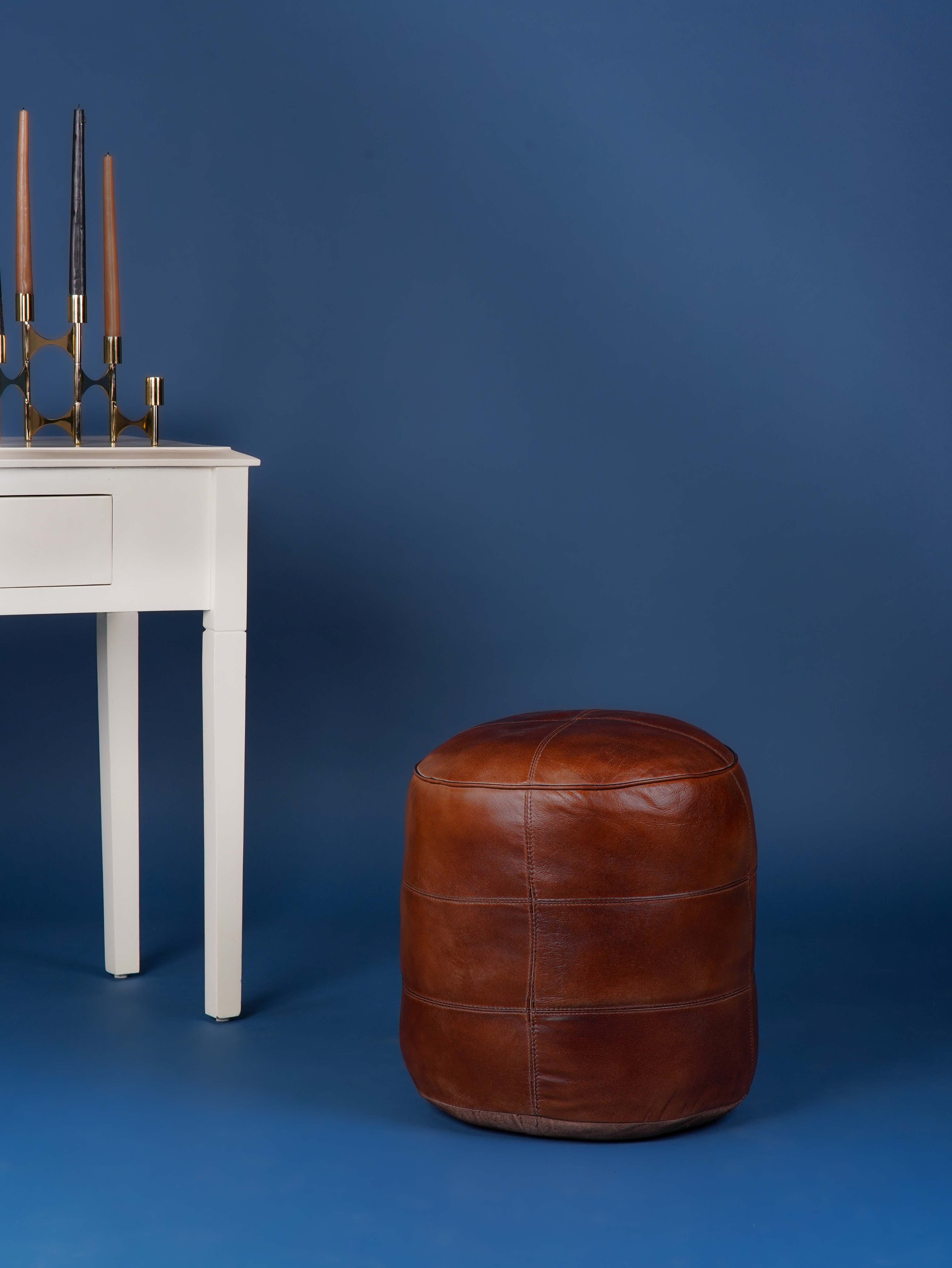 Round brown leather pouf next to white console table on blue background