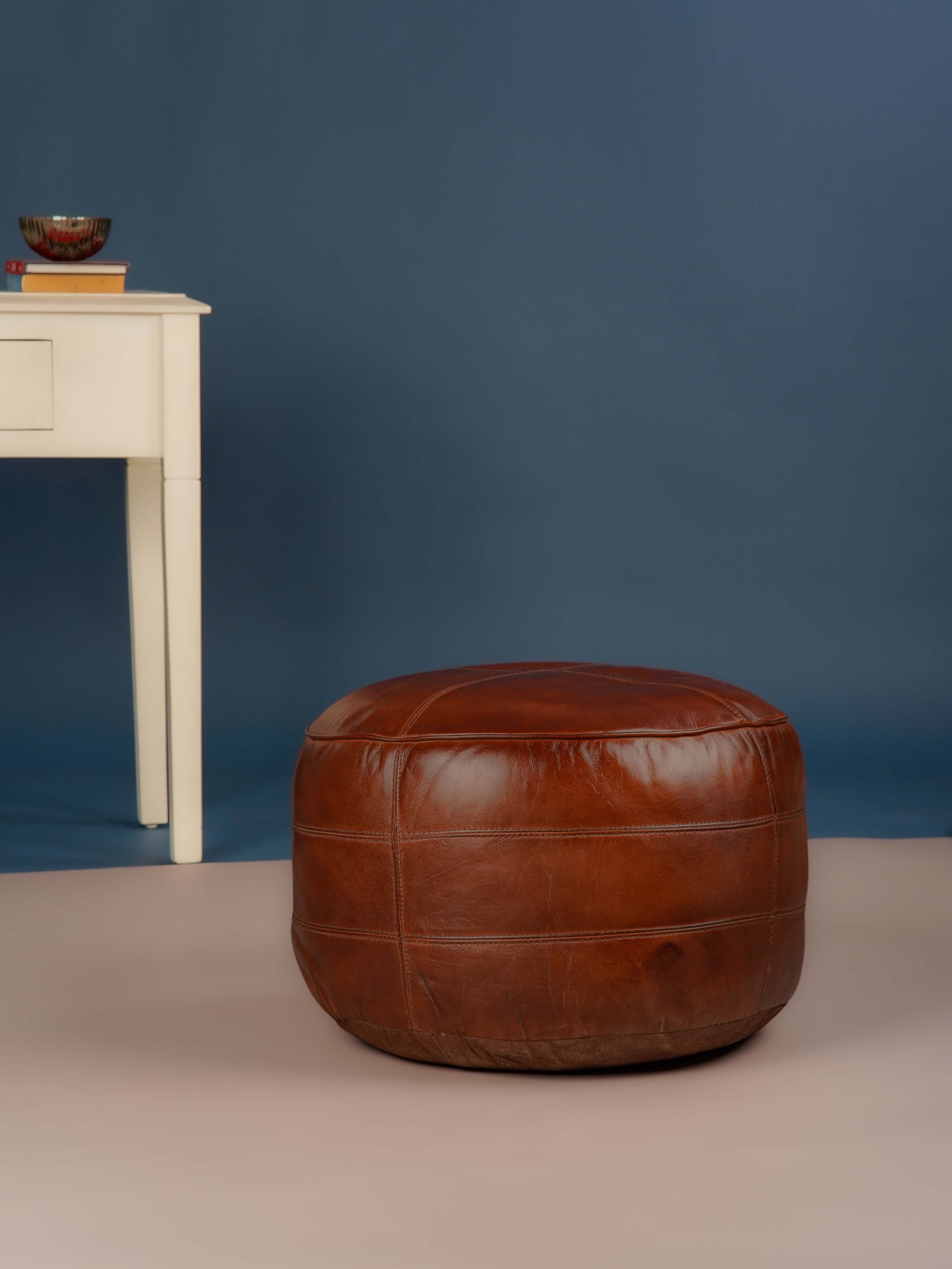 Round brown leather pouf next to white console table on blue background