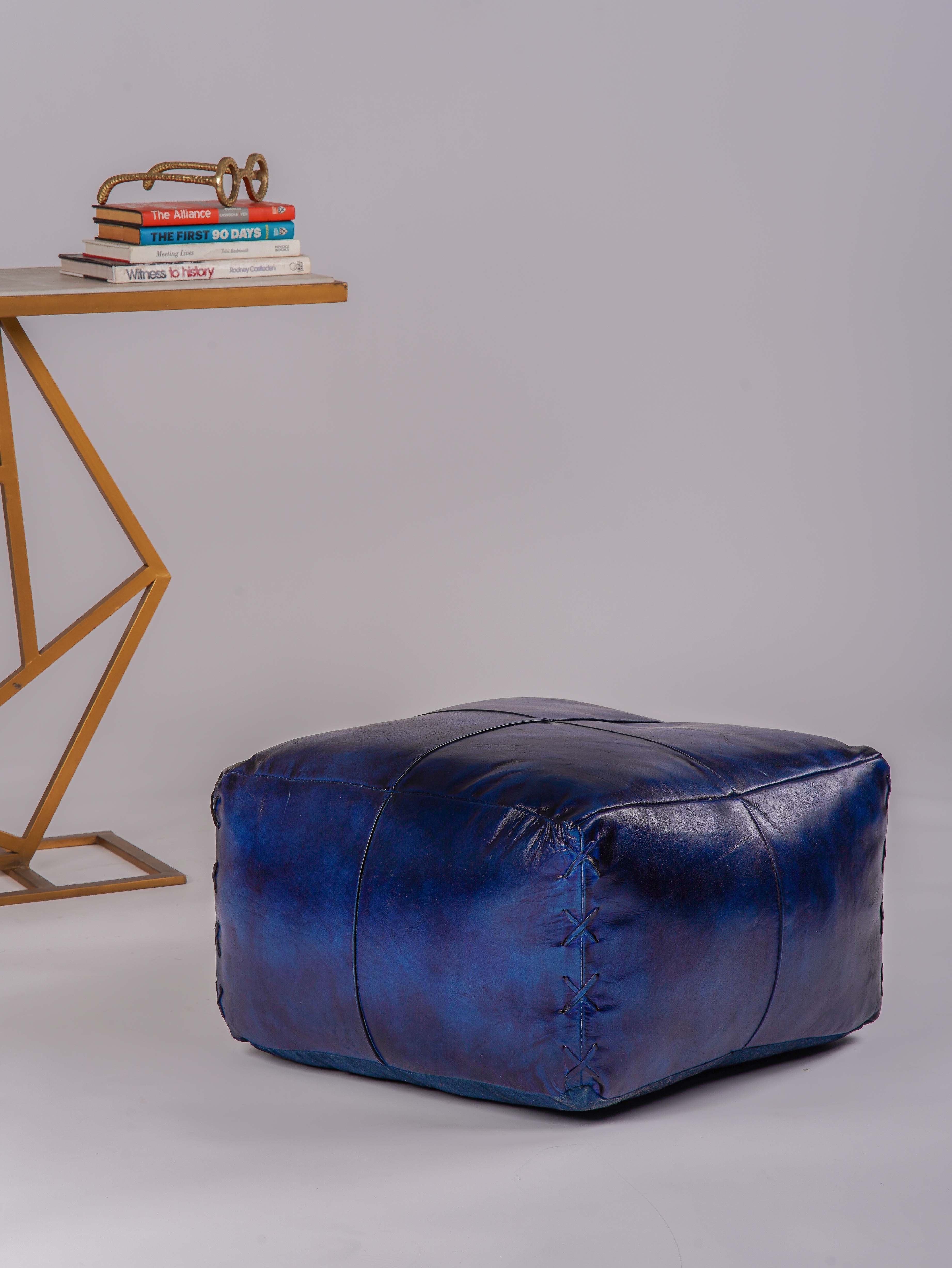 Square blue buffalo leather pouf beside modern gold accent table
