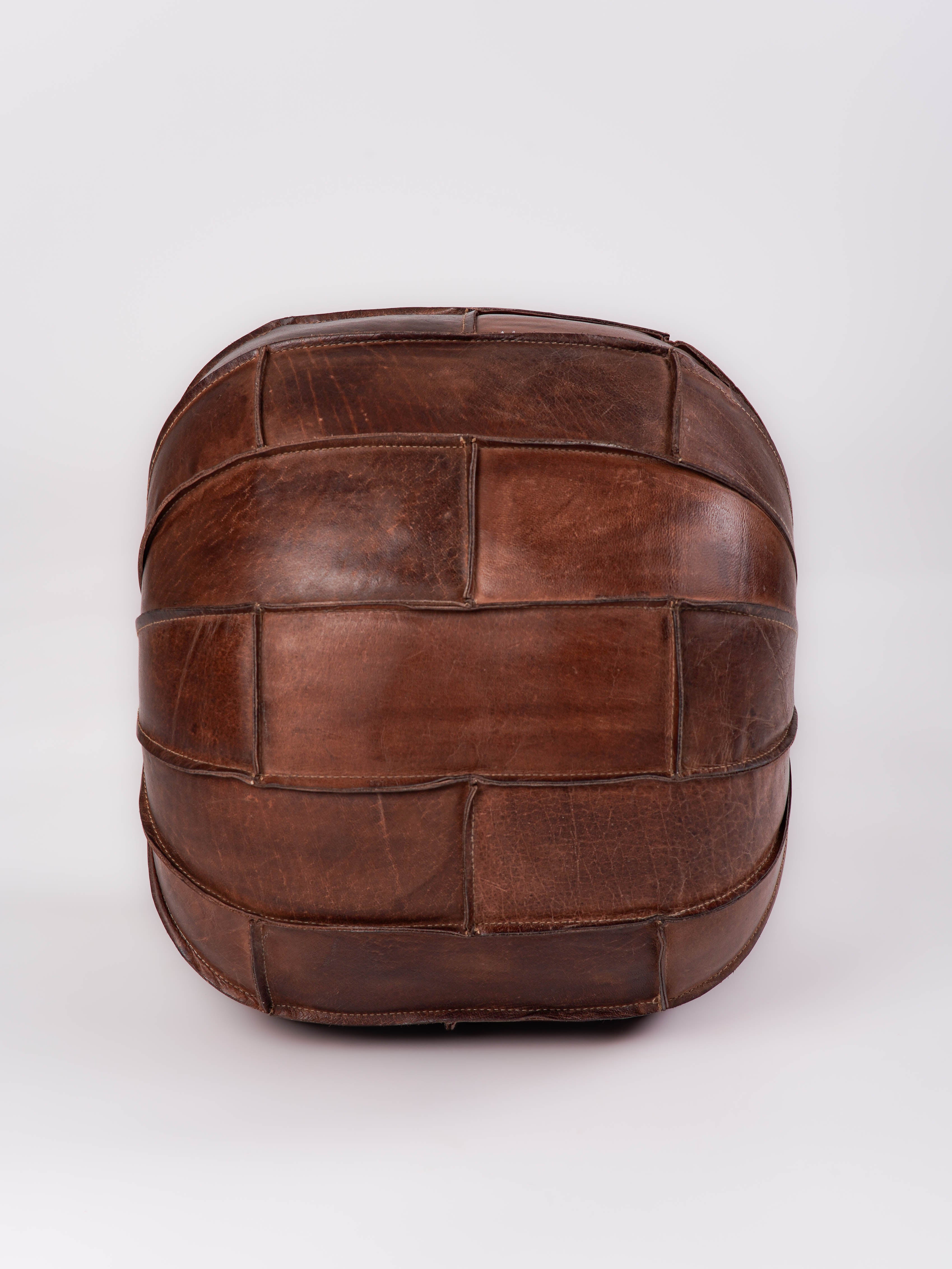 Structured round pouf in black buffalo leather next to beige sofa