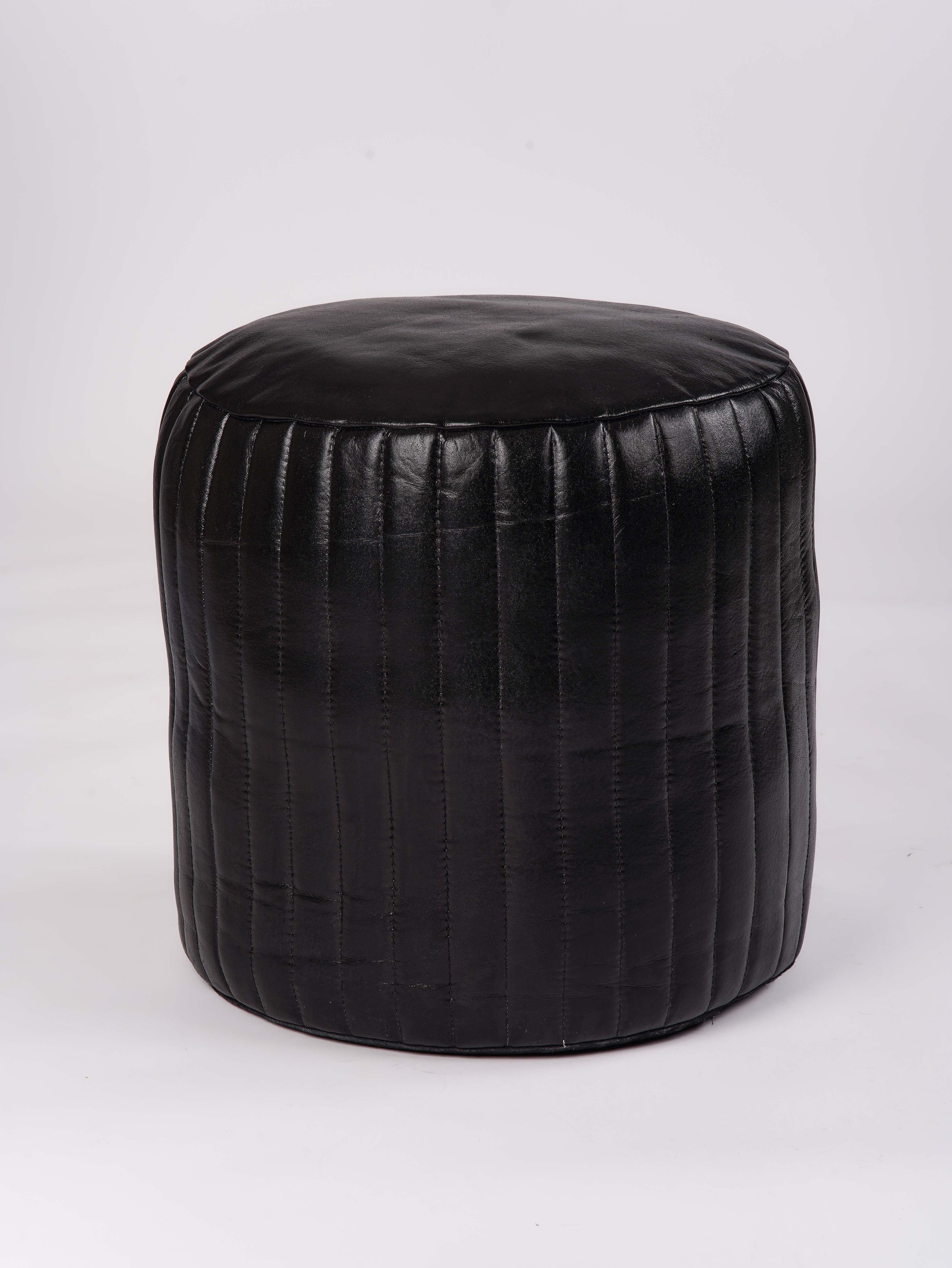 Soft black leather ottoman in round shape placed near bookshelf