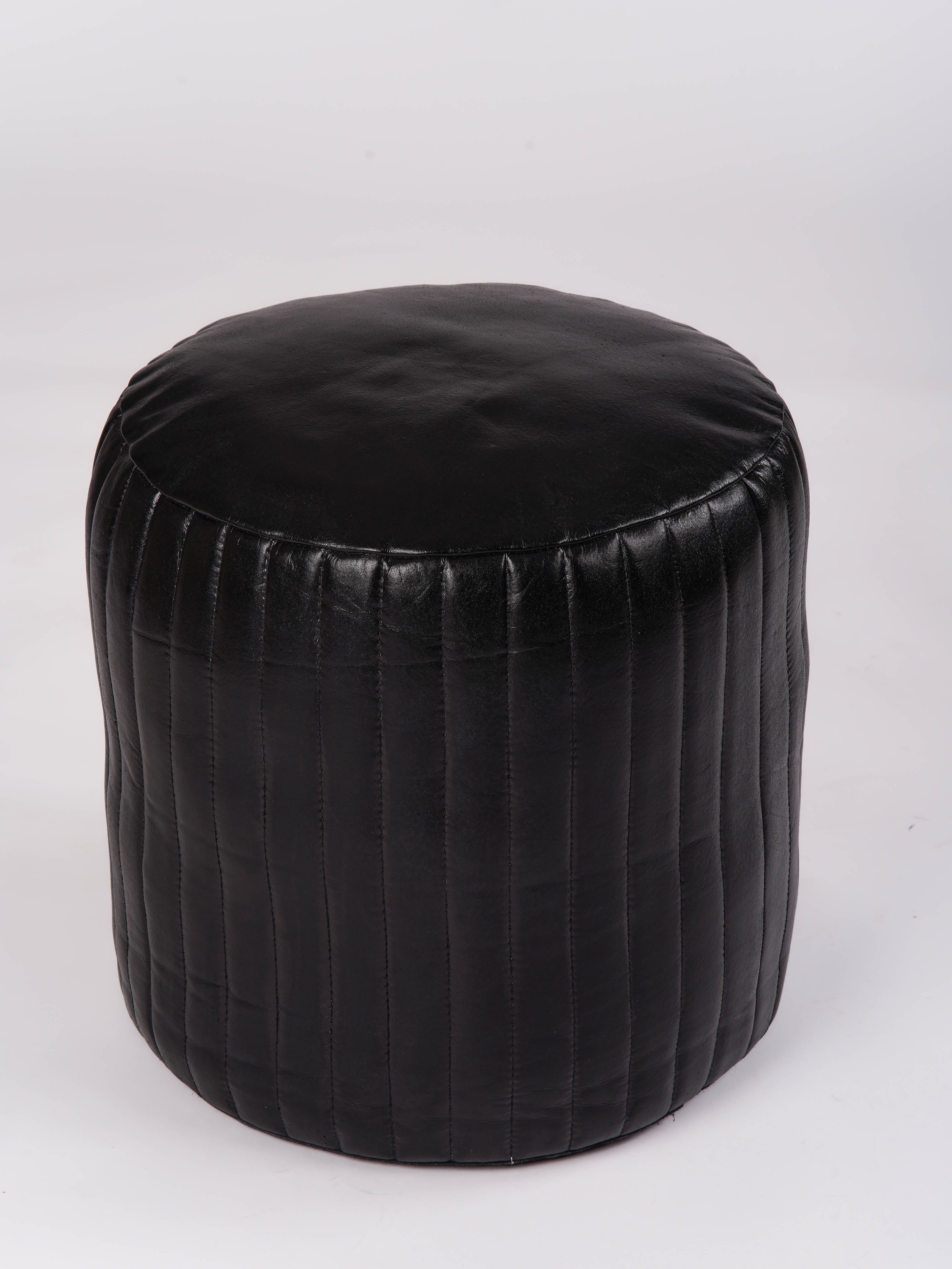 Soft black leather ottoman in round shape placed near bookshelf