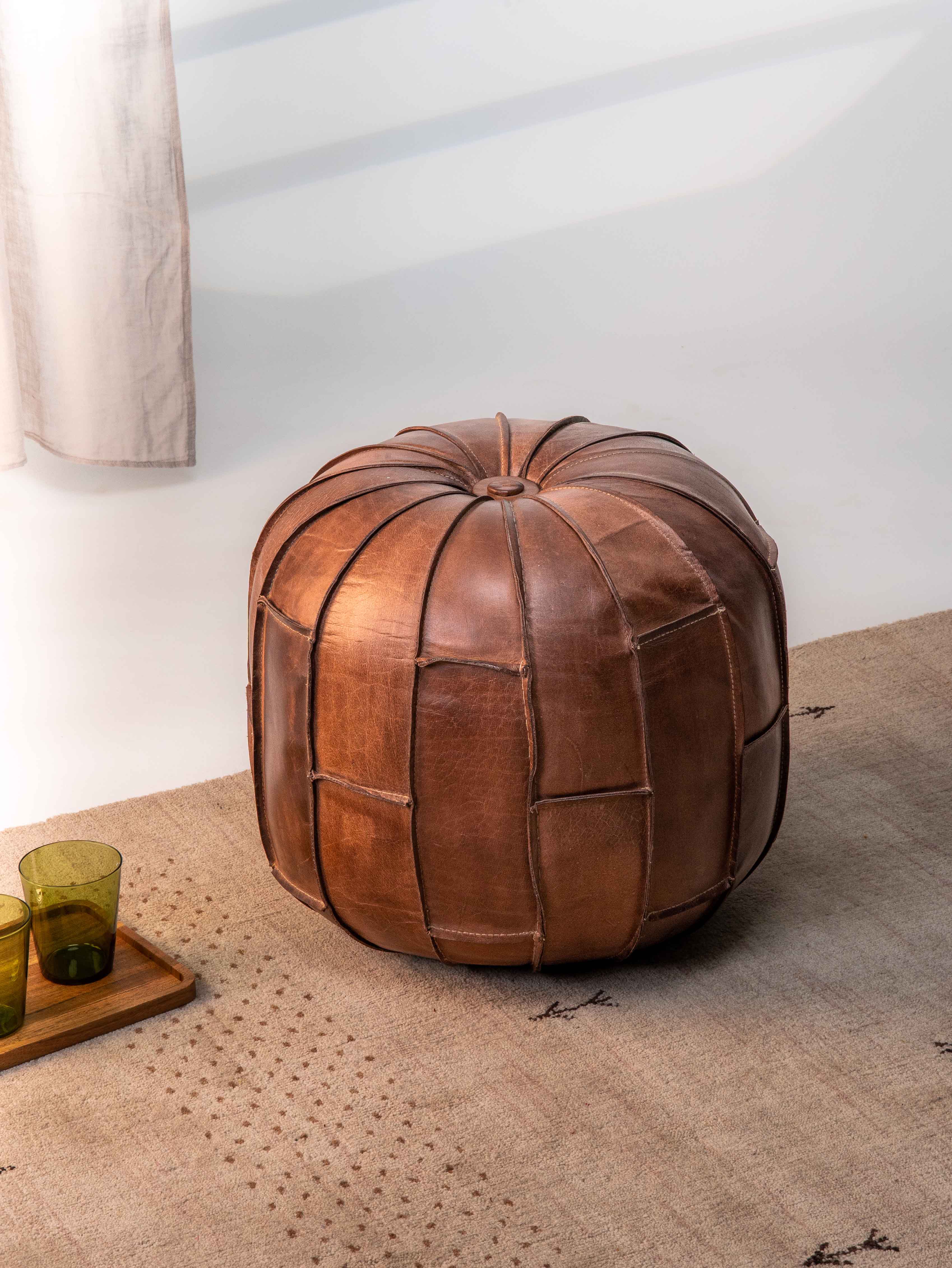 Round black buffalo leather pouf placed in modern living room setting