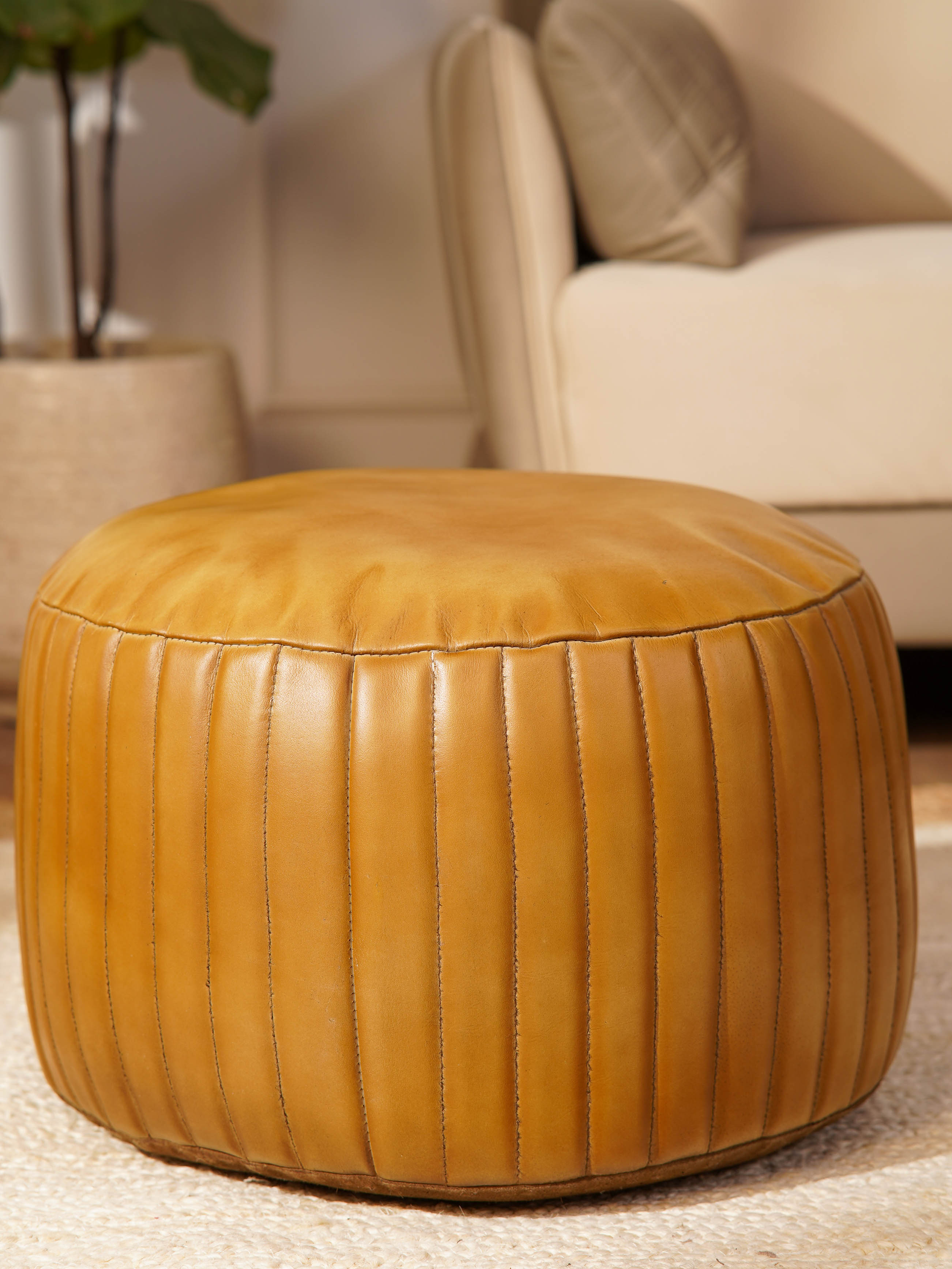 Cylindrical pouf with vertical stitched panels and natural leather finish