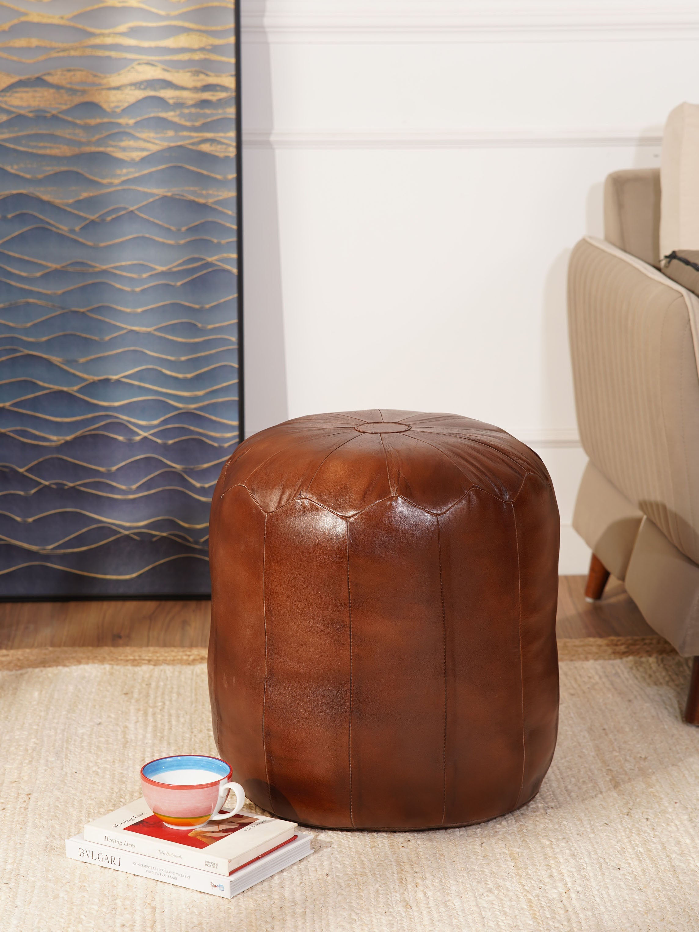 Round brown buffalo leather pouf in living room next to armchair