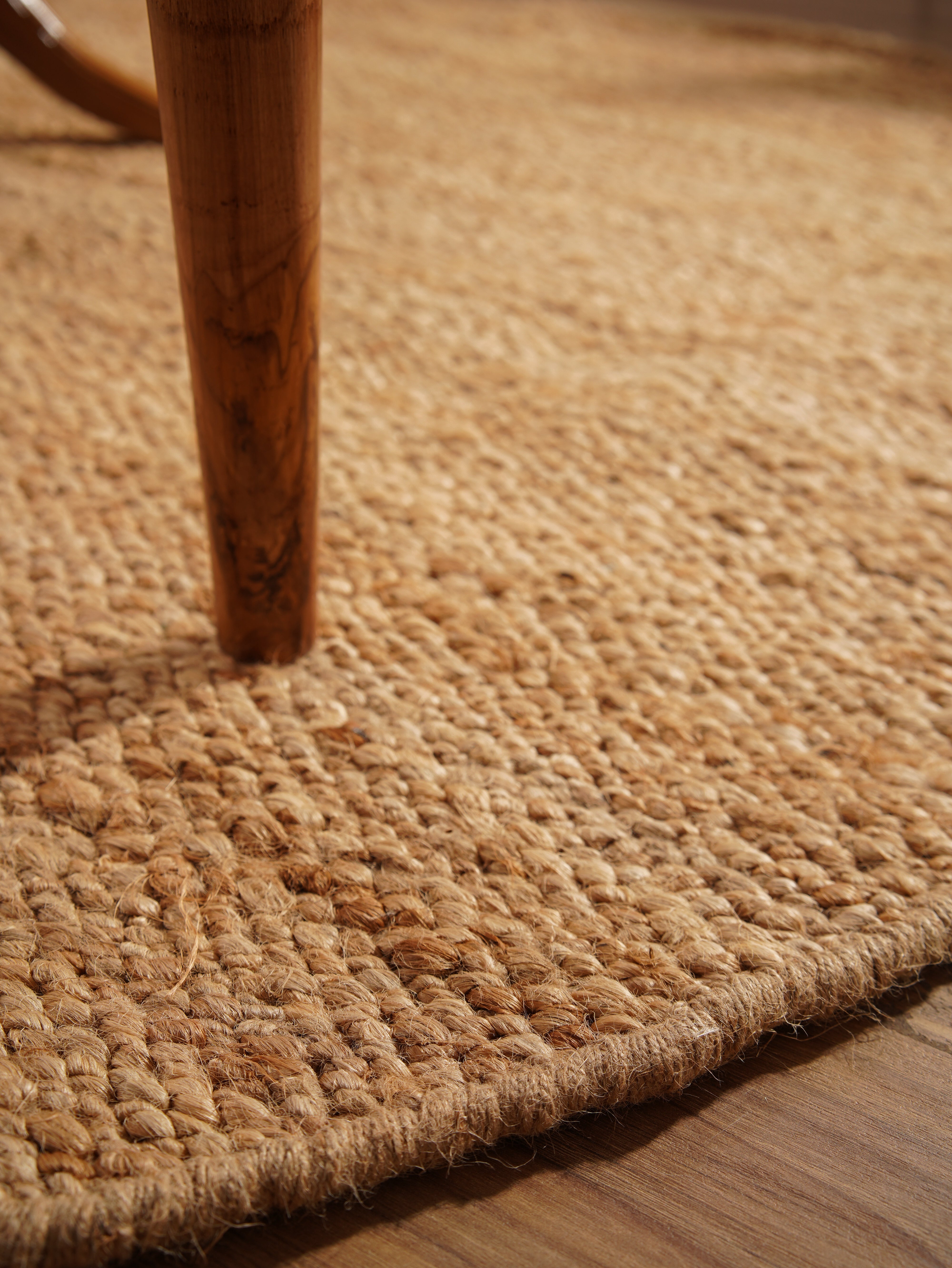 Side view of light brown handwoven jute rug under coffee table.