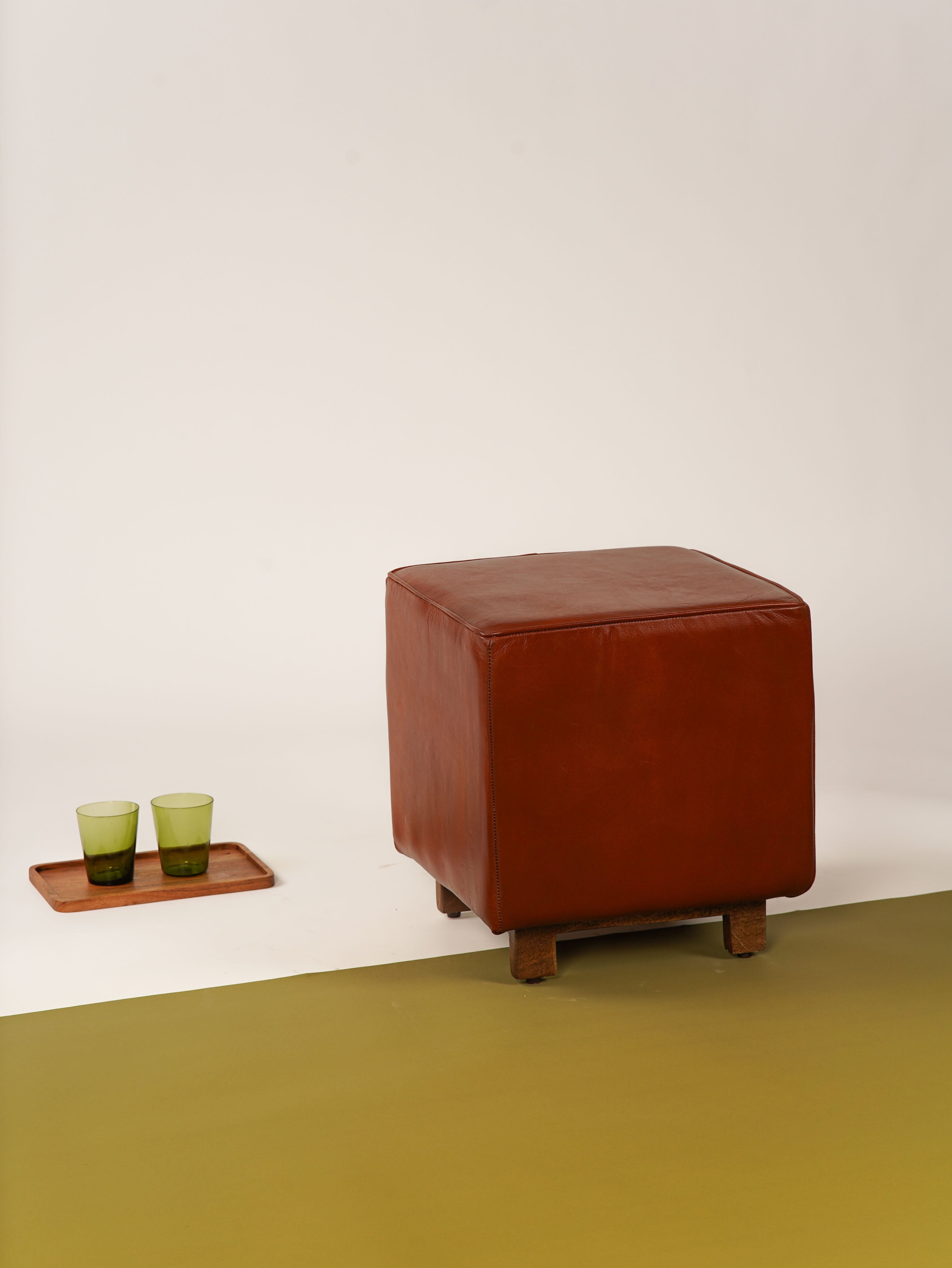 Brown buffalo leather stool with wood legs beside neutral-toned couch