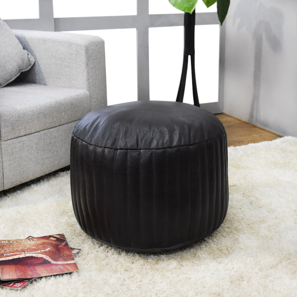 Round black buffalo leather pouf in modern room with yellow backdrop