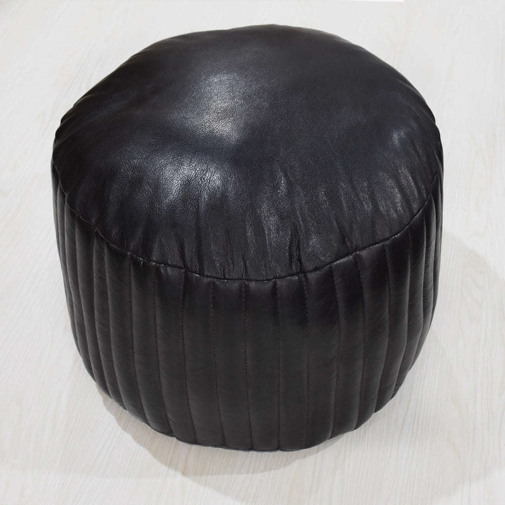 Soft black leather ottoman in round shape placed near bookshelf