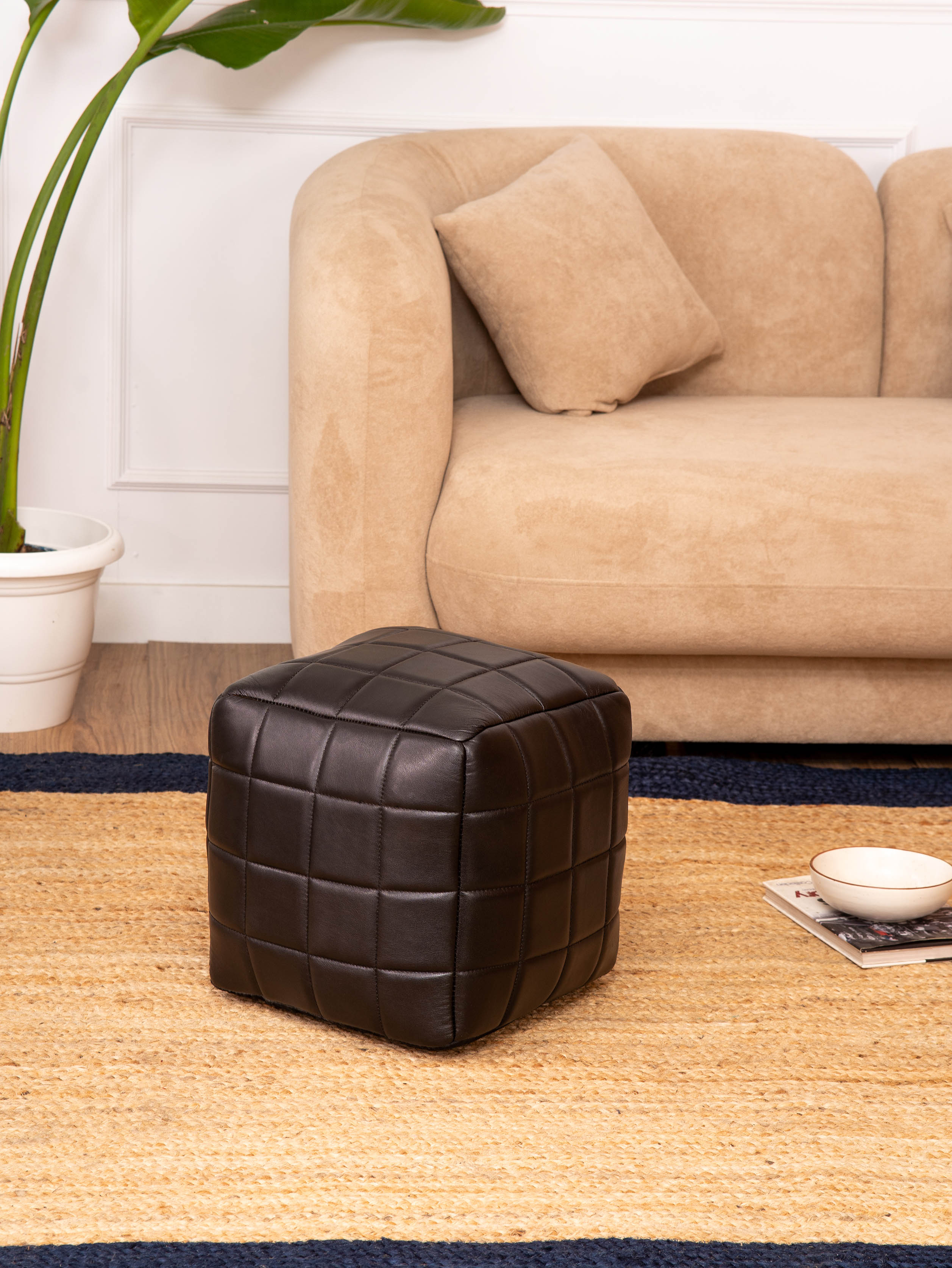 Black leather square pouf in bright room with beige sofa
