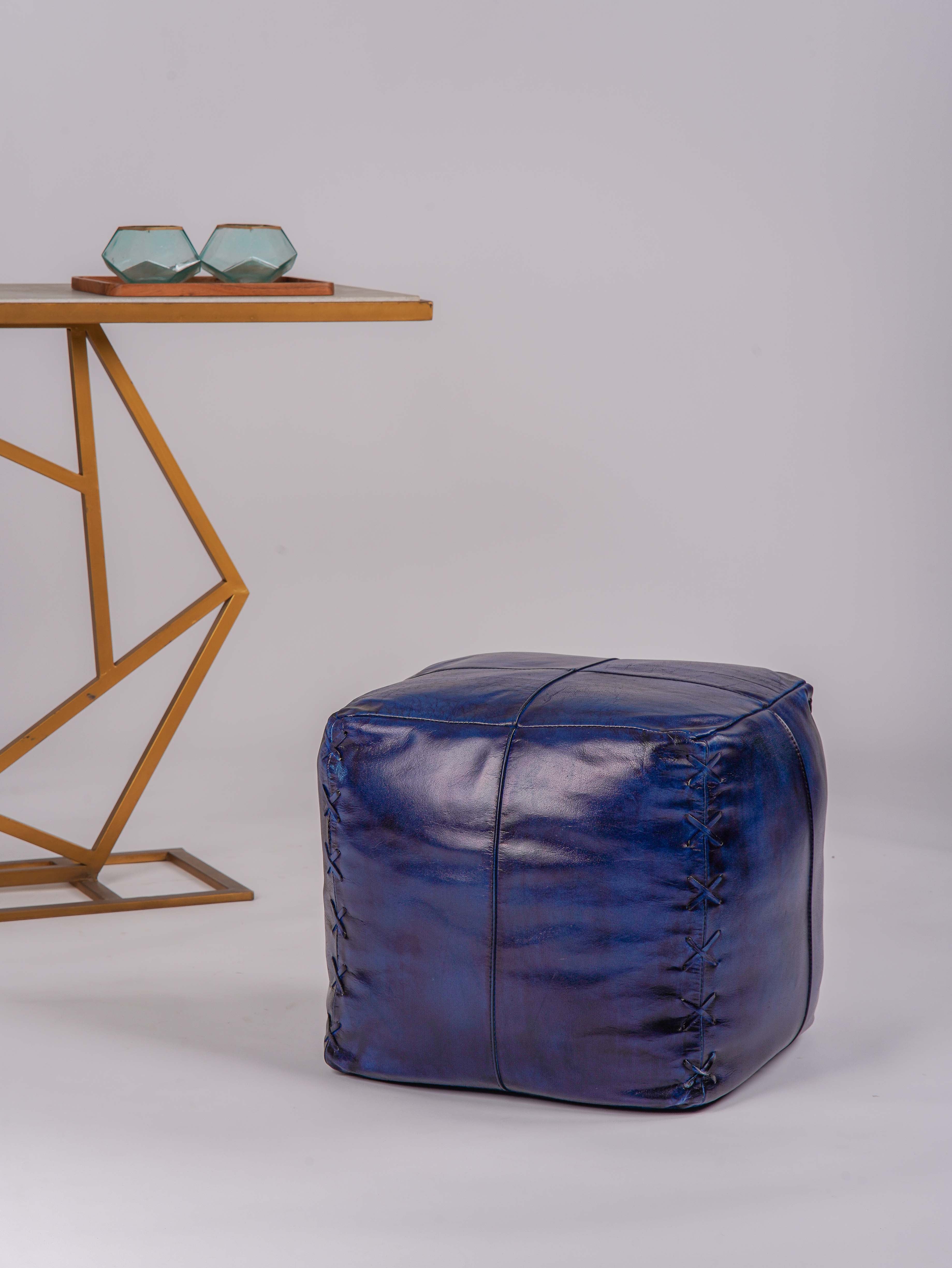 Square blue buffalo leather pouf beside modern gold accent table
