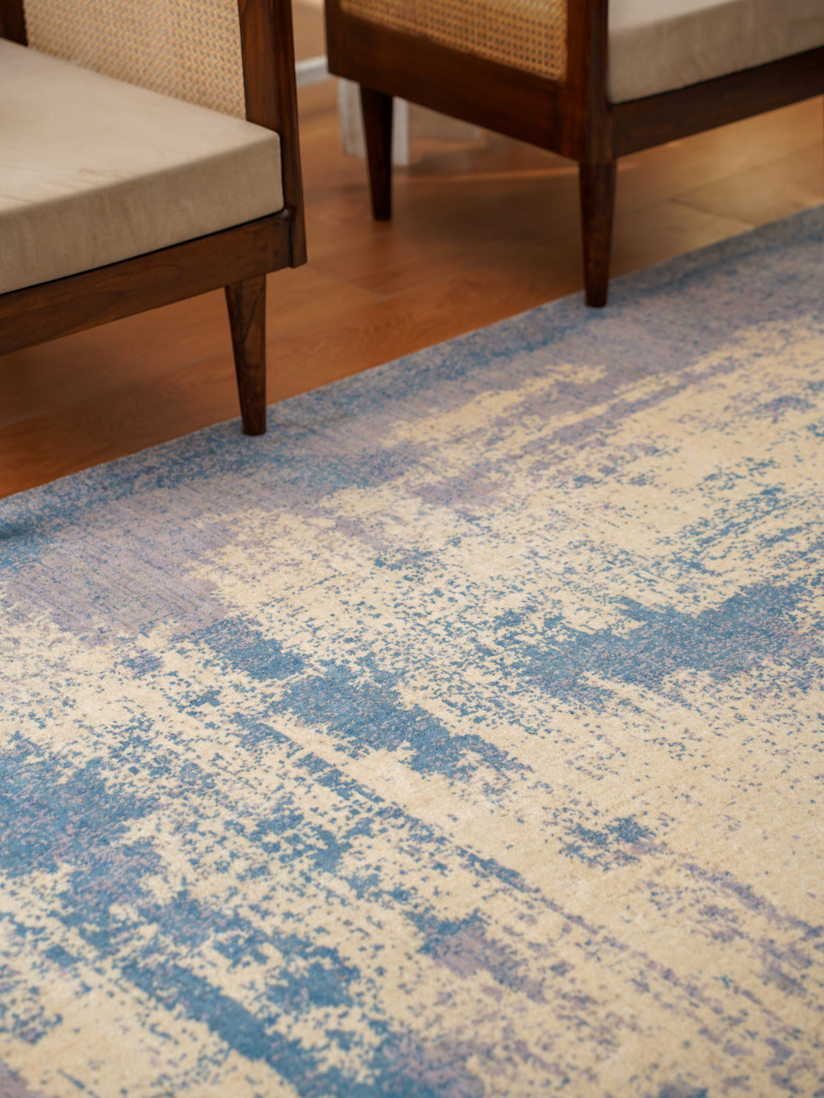 Close-up of a blue and beige patterned rug in a room with wooden chairs.