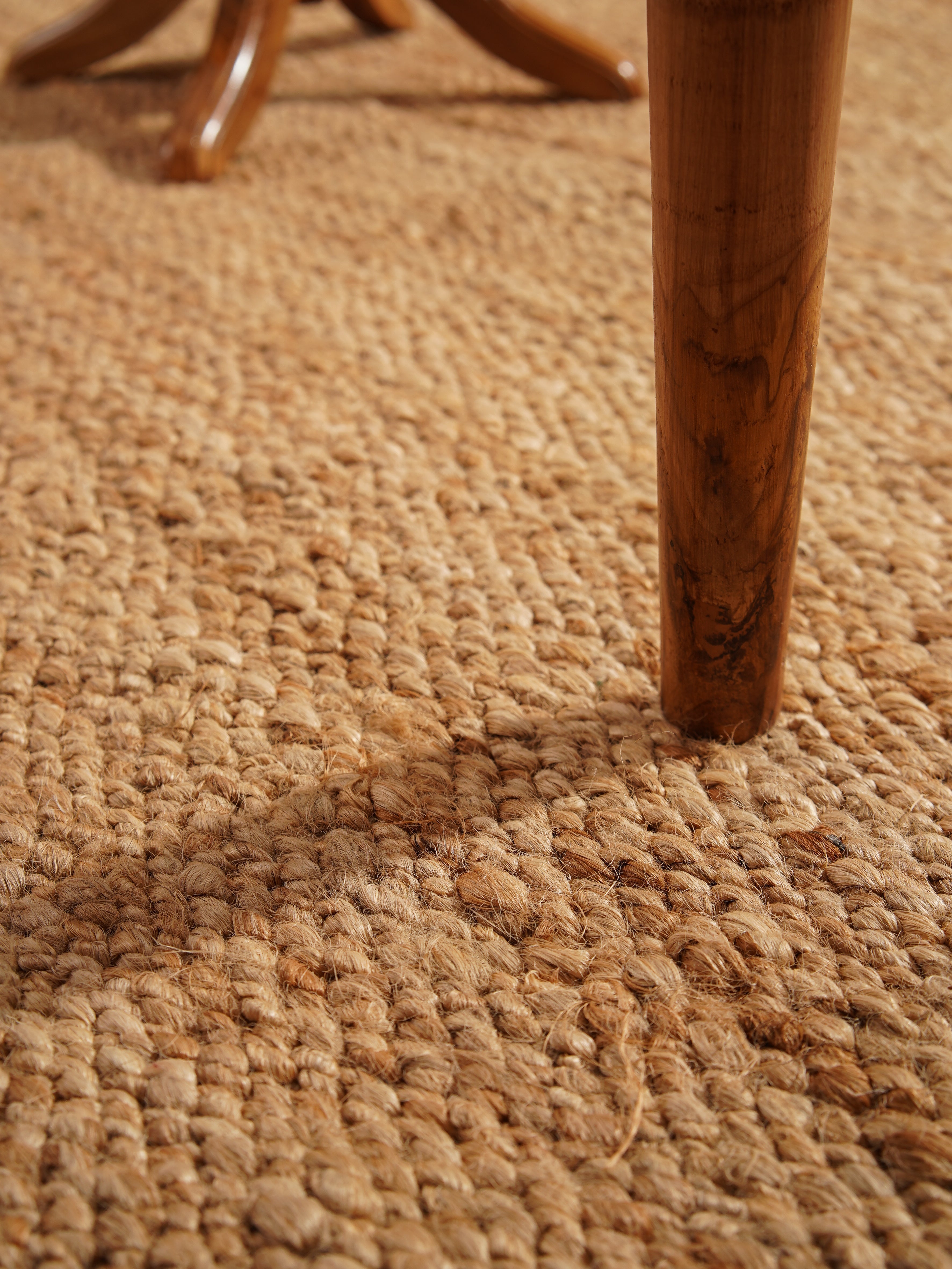 Side view of light brown handwoven jute rug under coffee table. 